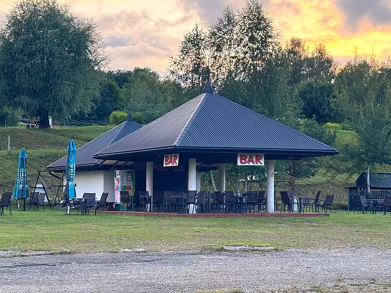 Altana baru z szyldami BAR i taras ze stolikami na terenie ośrodka o zachodzie słońca